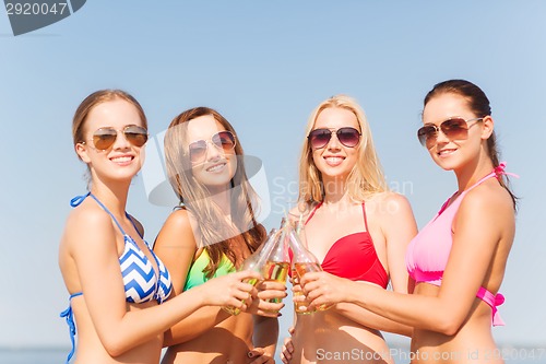 Image of group of smiling young women drinking on beach