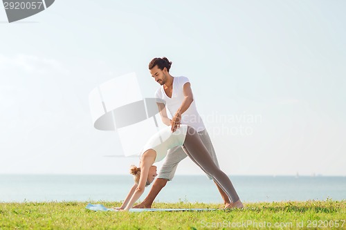 Image of smiling couple making yoga exercises outdoors