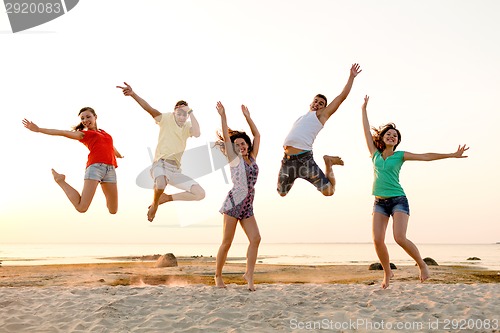 Image of smiling friends dancing and jumping on beach