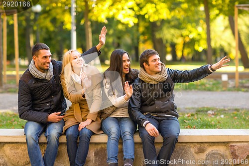 Image of group of smiling friends waving hands in city park