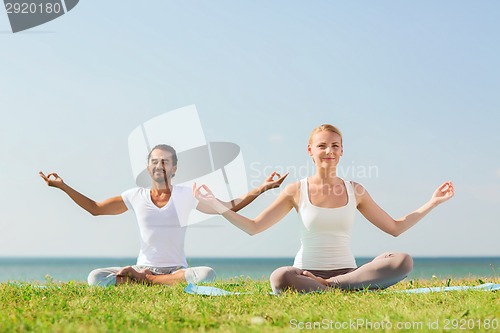 Image of smiling couple making yoga exercises outdoors