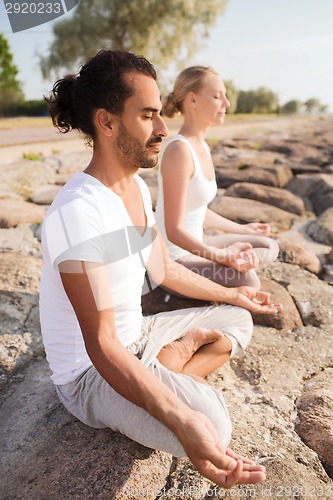 Image of smiling couple making yoga exercises outdoors