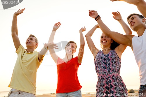 Image of smiling friends dancing on summer beach