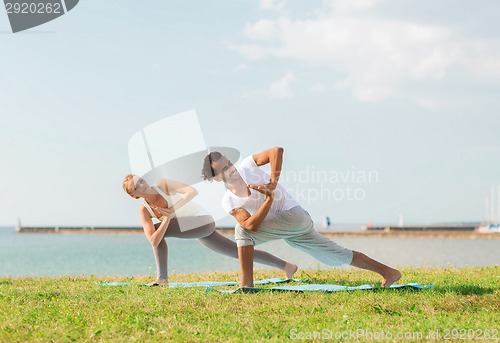 Image of smiling couple making yoga exercises outdoors