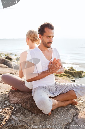 Image of smiling couple making yoga exercises outdoors