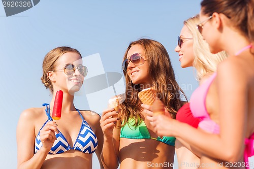 Image of group of smiling women eating ice cream on beach