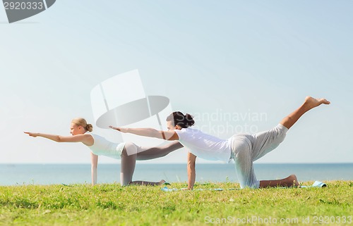 Image of smiling couple making yoga exercises outdoors