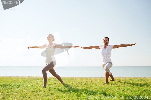 Image of smiling couple making yoga exercises outdoors