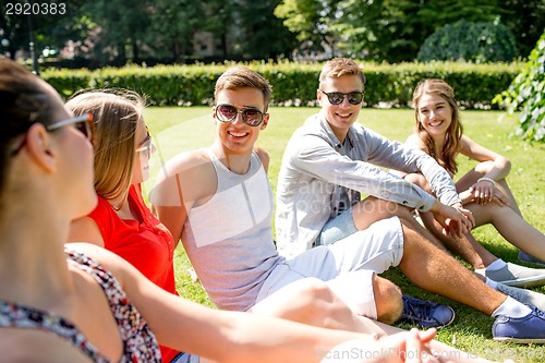 Image of group of smiling friends outdoors sitting in park