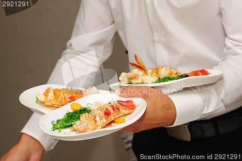 Image of Waiter holds plates with lobsters