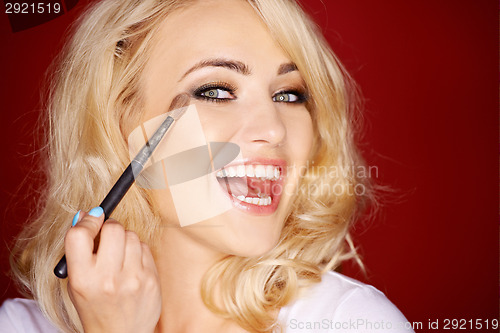 Image of Laughing beautiful woman applying blusher