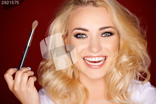 Image of Laughing beautiful woman applying blusher