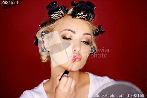 Image of Woman applying makeup with her hair in curlers