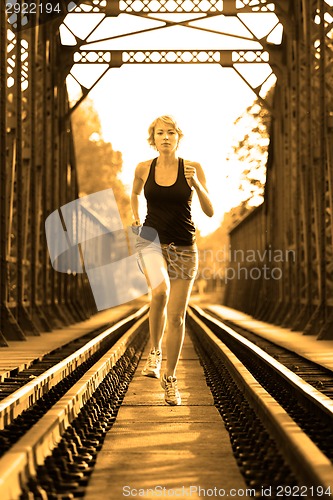 Image of Active female athlete running on railaway tracks.