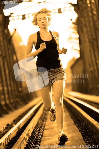 Image of Active female athlete running on railaway tracks.