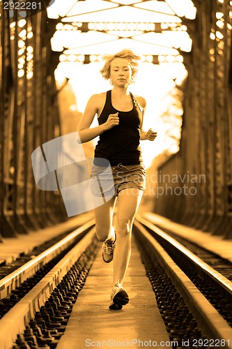 Image of Active female athlete running on railaway tracks.