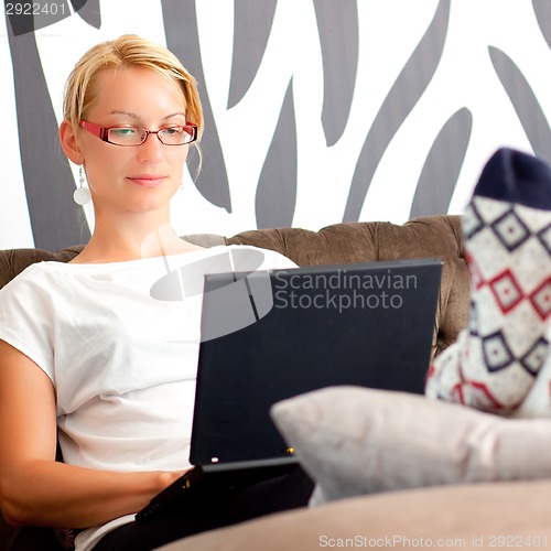 Image of Beautiful young lady sitting on sofa, using laptop