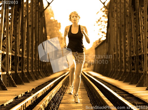 Image of Active female athlete running on railaway tracks.