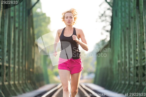 Image of Active female athlete running on railaway tracks.