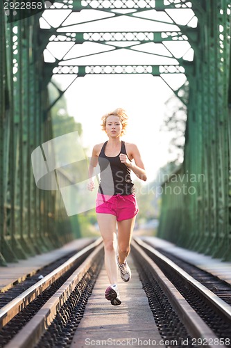 Image of Active female athlete running on railaway tracks.