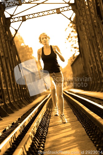 Image of Active female athlete running on railaway tracks.