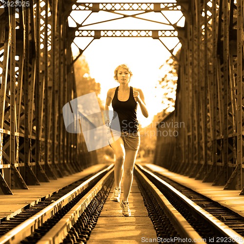 Image of Active female athlete running on railaway tracks.