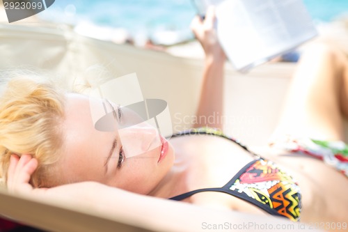 Image of Thoughtful woman lies on hammock on the beach.