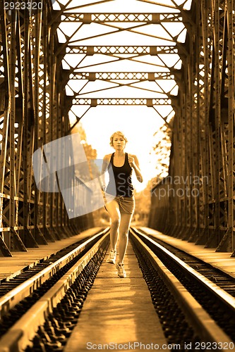 Image of Active female athlete running on railaway tracks.