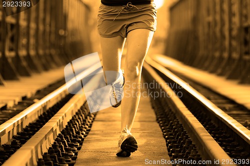 Image of Active female athlete running on railaway tracks.