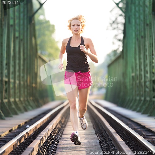 Image of Active female athlete running on railaway tracks.