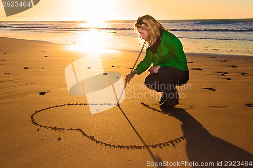 Image of Woman drowing a heart shape in the sand.