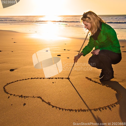 Image of Woman drowing a heart shape in the sand.