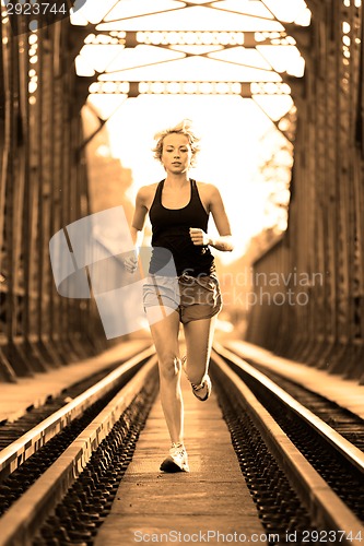 Image of Active female athlete running on railaway tracks.