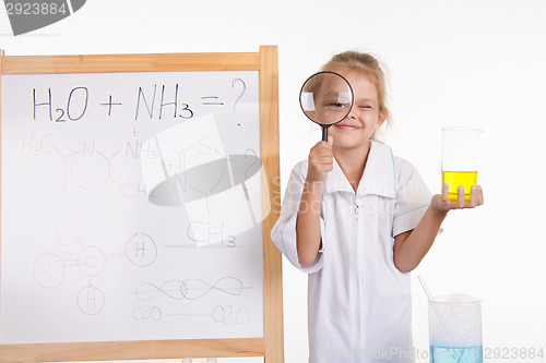 Image of Girl chemist flask and magnifying glass at the blackboard