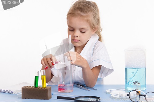 Image of Schoolgirl pouring red liquid a flask in chemistry class