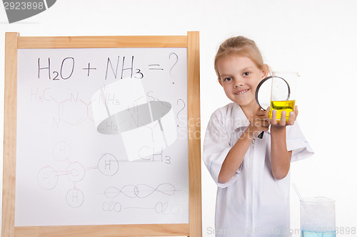 Image of Girl chemist examines liquid in flask under a magnifying glass