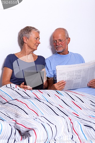 Image of Senior Couple with Tablet and Newspaper in Bed