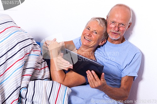 Image of Senior Couple with Tablet and Newspaper in Bed