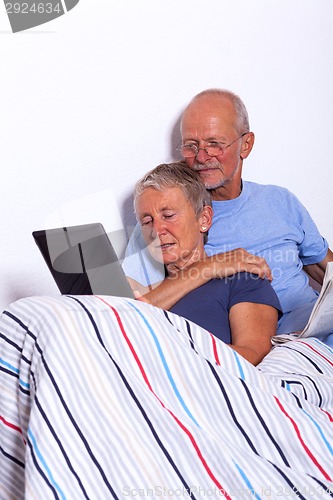 Image of Senior Couple with Tablet and Newspaper in Bed