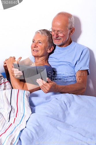 Image of Senior Couple with Tablet and Newspaper in Bed