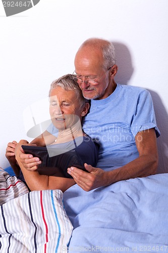 Image of Senior Couple with Tablet and Newspaper in Bed