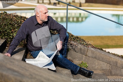 Image of Man sitting on steps reading a newspaper