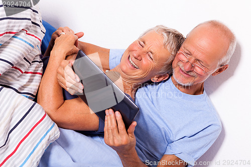 Image of Senior Couple with Tablet and Newspaper in Bed