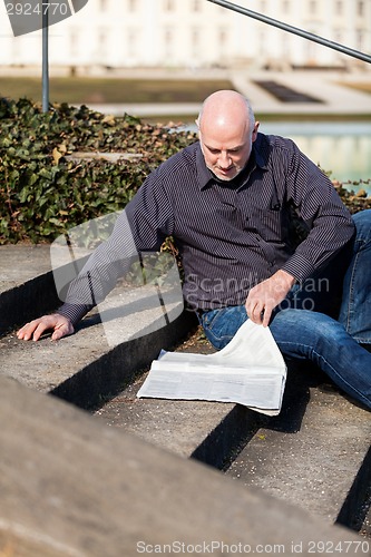 Image of Man sitting on steps reading a newspaper