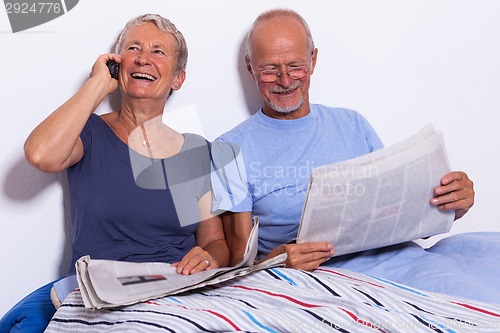 Image of Senior Couple with Tablet and Newspaper in Bed