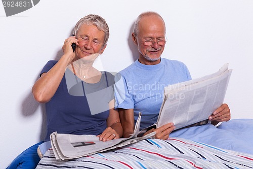 Image of Senior Couple with Tablet and Newspaper in Bed