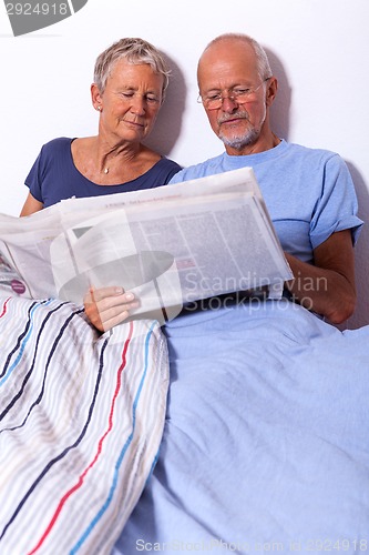 Image of Senior Couple with Tablet and Newspaper in Bed