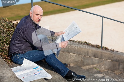 Image of Man sitting on steps reading a newspaper