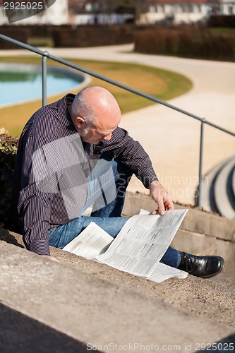 Image of Man sitting on steps reading a newspaper