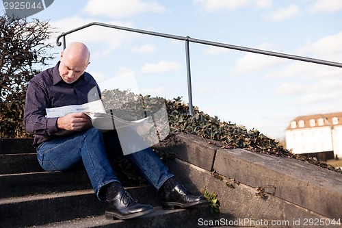 Image of Man sitting on steps reading a newspaper